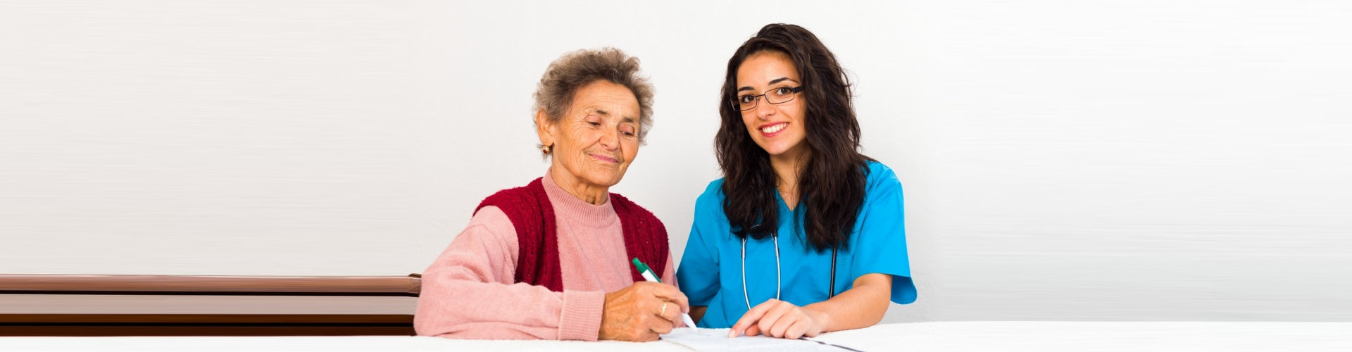 an elderly woman holding a pen with a female caregiver